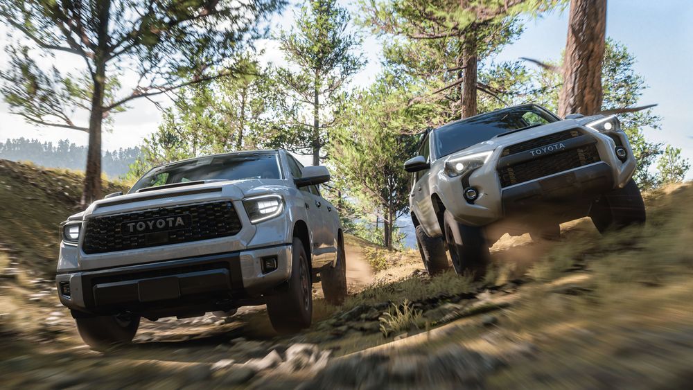 A pair of white Toyota TRD Pro trucks drive through trees in a forest.