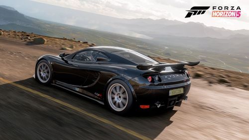 Black sports car zooming down the edge of a road with a barren landscape behind it.