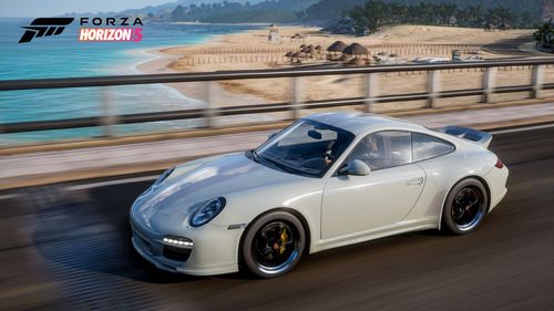 A silver Porsche 911 Sport Classic zooms across a bridge at high-speed with stunning views of the beach and seawater in the backdrop.