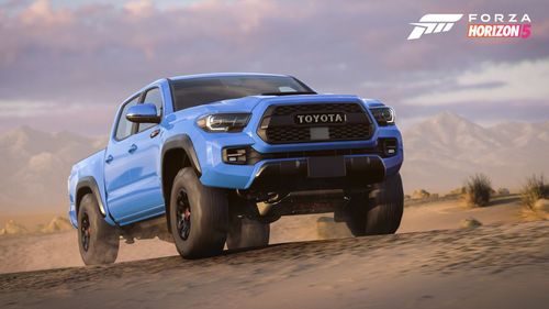 A blue Toyota Tacoma TRD Pro drives through a sand desert.