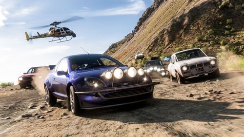 The Racing Puma and other rally cars race on a mountain while a helicopter flies overhead.