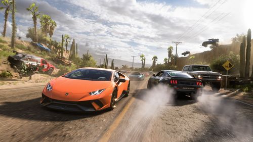 A pack of supercars led by an orange Lamborghini drives past a drifting Ford Mustang and off-roaders heading in the opposite direction, all in Mexico's desert surrounded by cacti and beach trees.